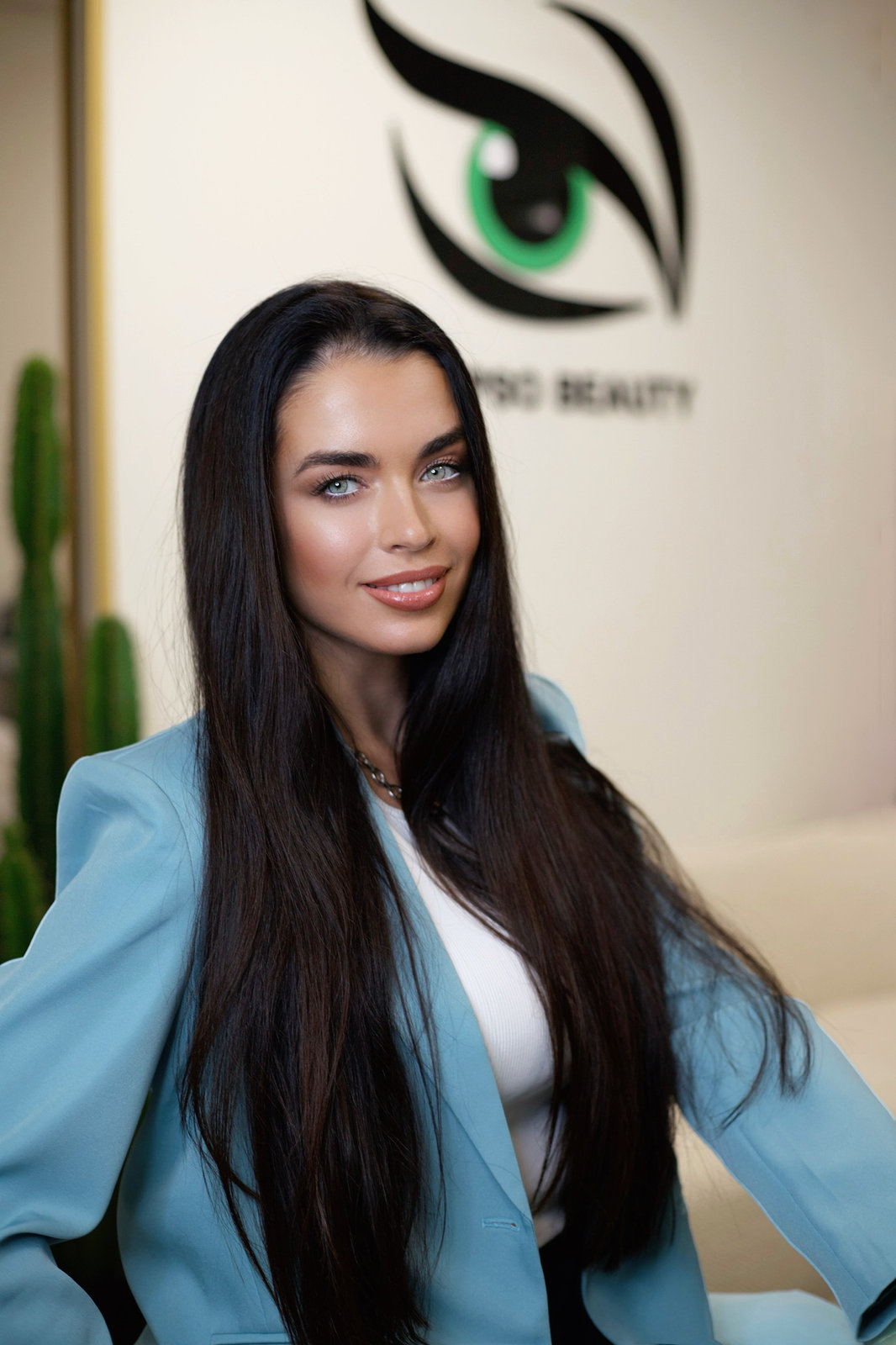 Yulia Alpeza, founder of Calypso Beauty, in a blue blazer in front of the studio’s logo wall