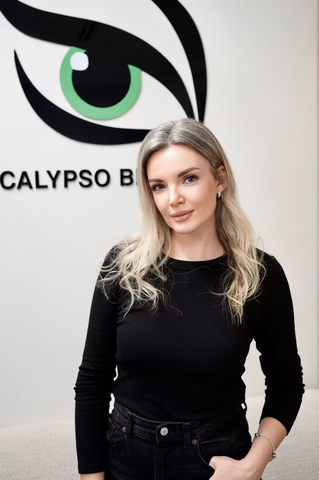 Portrait of Yana Glinkina, sugaring specialist, in front of the Calypso Beauty logo wall
